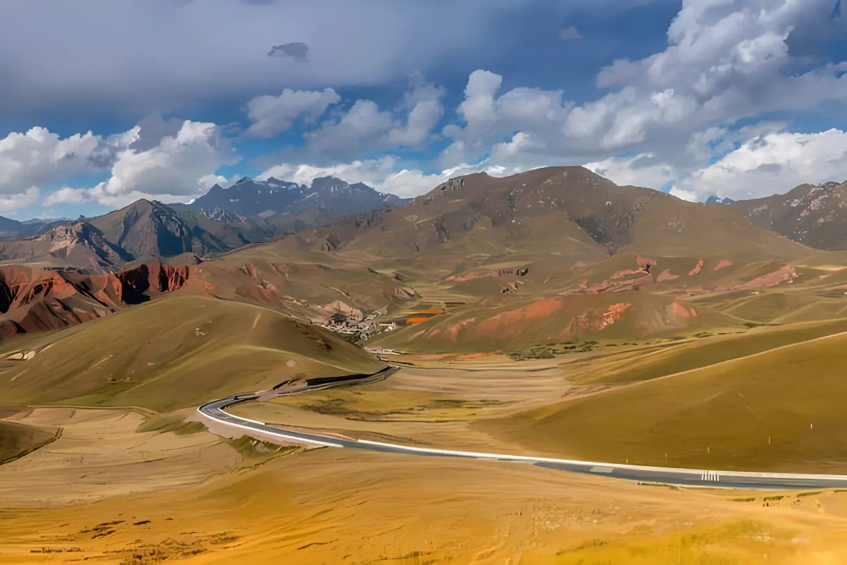 这张图片展示了一条蜿蜒的公路穿越广阔的草原和多彩的山脉，天空中飘着几朵云。