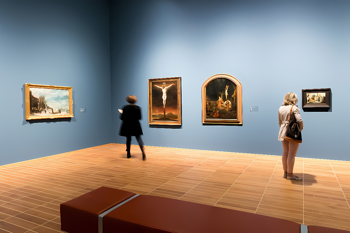 两位观众在画廊内欣赏挂在深蓝色墙壁上的几幅精美油画，画廊内部设计简洁，光线柔和。
