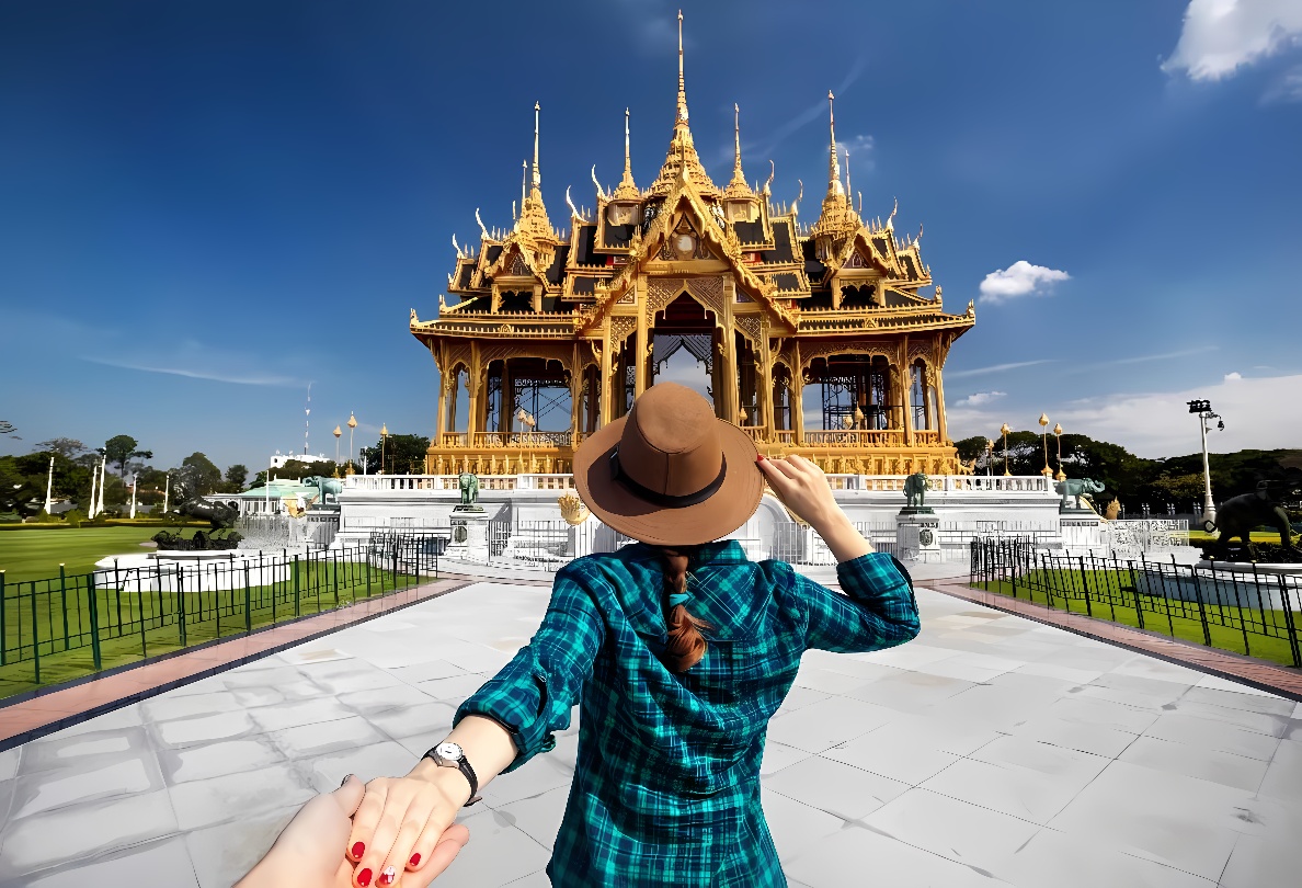 一位戴着帽子的女士背对镜头，穿格子衫，似乎在牵着拍照者的手，面向金色华丽的宫殿，天空晴朗。