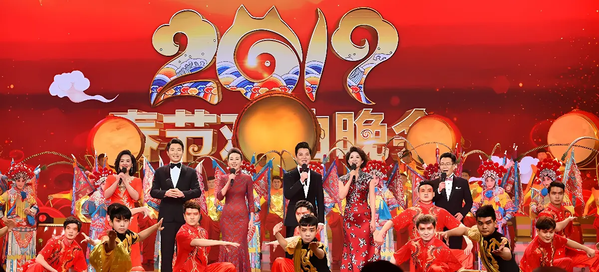这是一张春节联欢晚会的图片，舞台上多位身着节日盛装的演员在进行传统庆祝表演，气氛热烈，色彩鲜艳。
