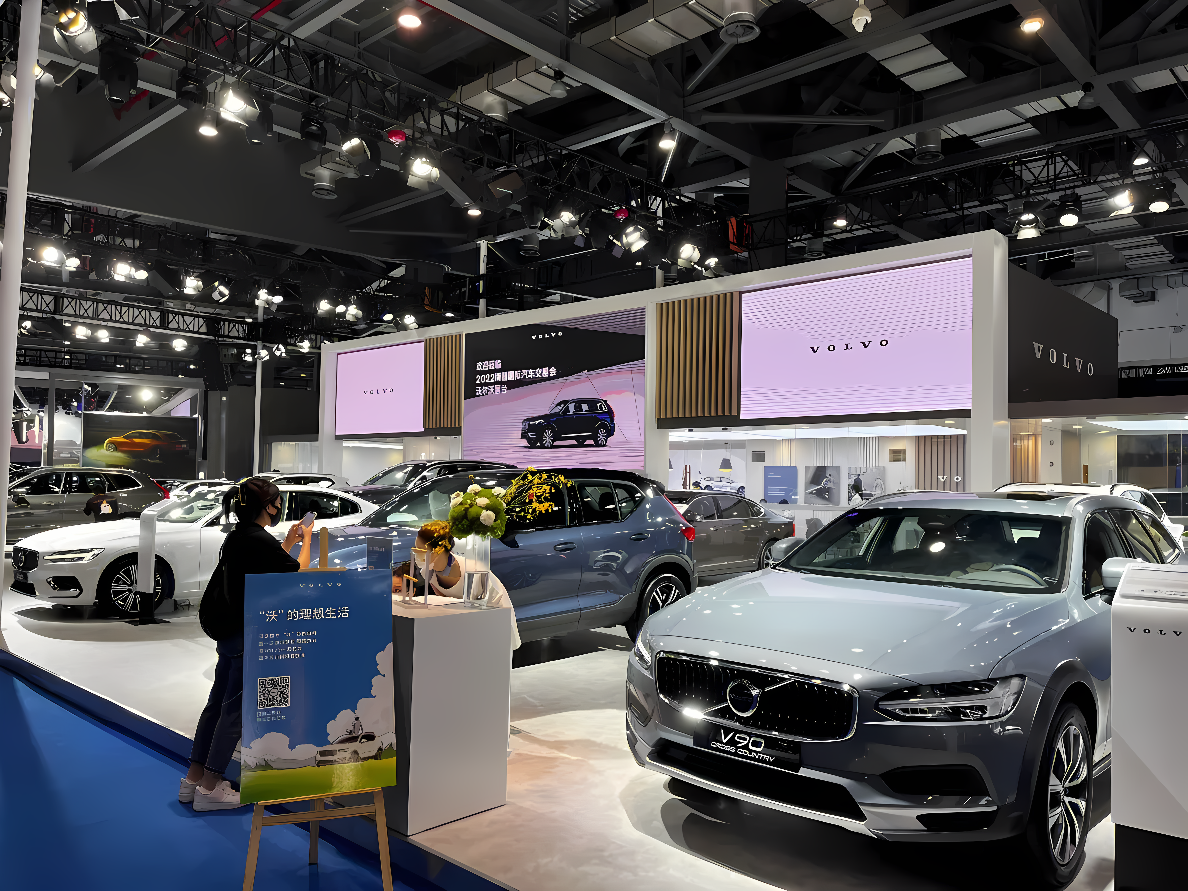 图片展示了一个汽车展览会场景，有多辆沃尔沃品牌汽车陈列，观众正在展台前参观，现场布置现代且专业。