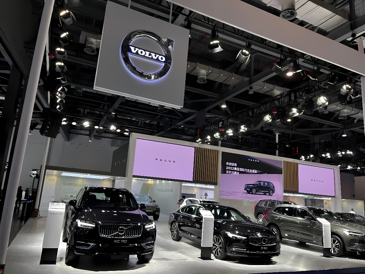 图片展示了沃尔沃品牌的汽车展台，几辆车型展出，大屏幕播放宣传，现场布置现代且专业。