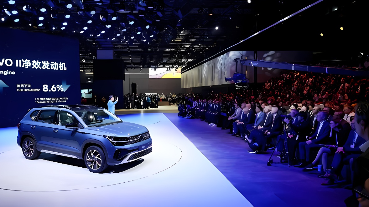 图片展示了一场车展，观众围坐在展台周围，一位演讲者在台上介绍一辆展出的新型蓝色汽车。