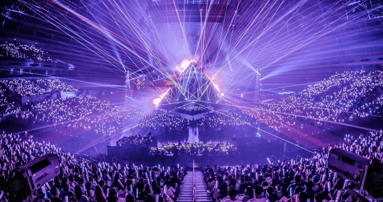 这是一场室内音乐会的现场，彩色的激光从舞台中央射出，观众群手持荧光棒，营造出热烈而梦幻的氛围。