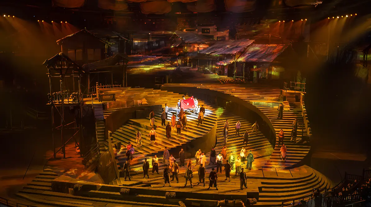 这是一张舞台剧照片，呈现多层次舞台设计，有多位表演者在舞台上，灯光营造出温暖气氛，场景布局复杂，色彩丰富。