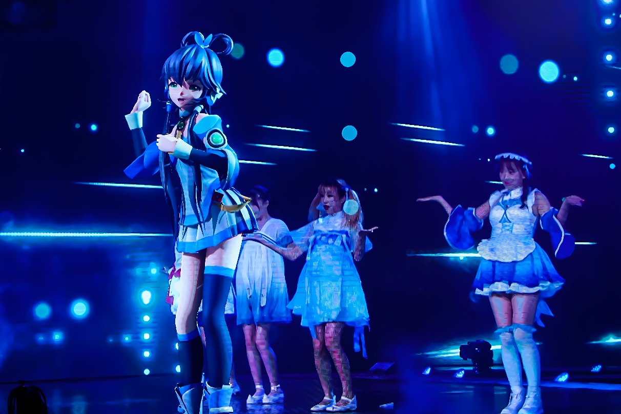 图片展示了一场舞台表演，主要是一位穿着现代服装的动画风格角色，背景是蓝色灯光和几位伴舞者。