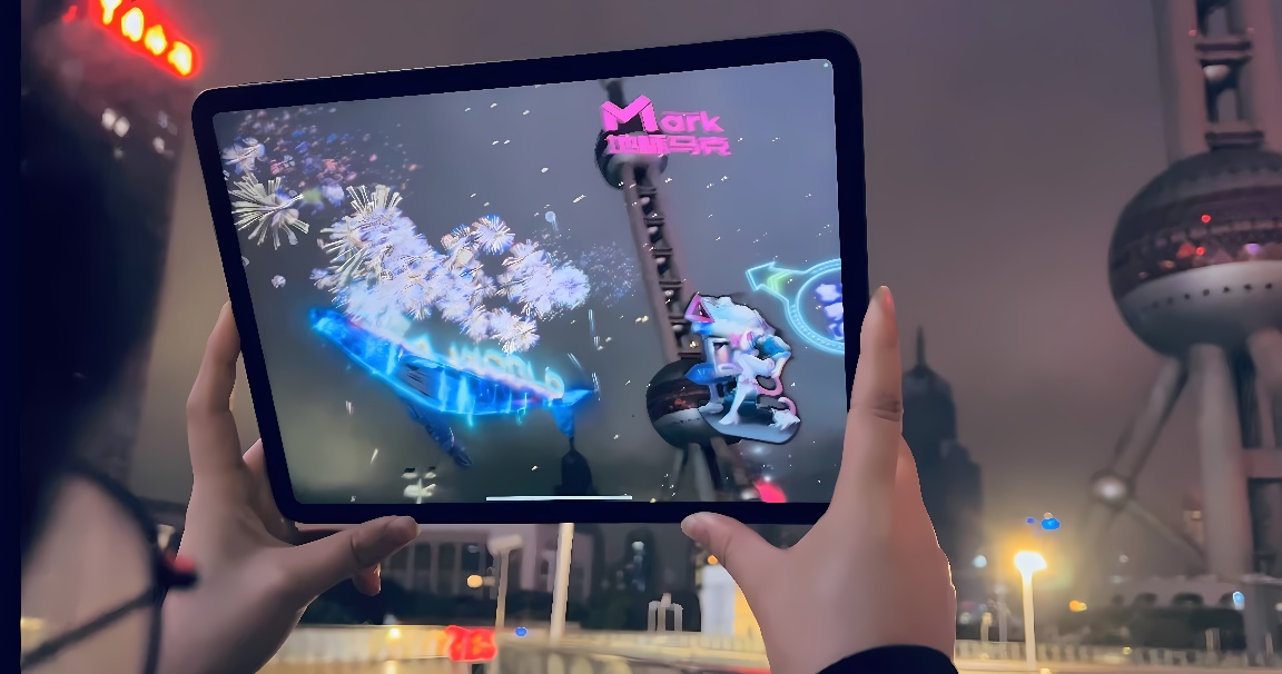 图片展示双手持平板电脑，屏幕上显示烟花和城市地标，背景为夜晚模糊的城市景观，灯光闪烁，氛围现代科技感强烈。