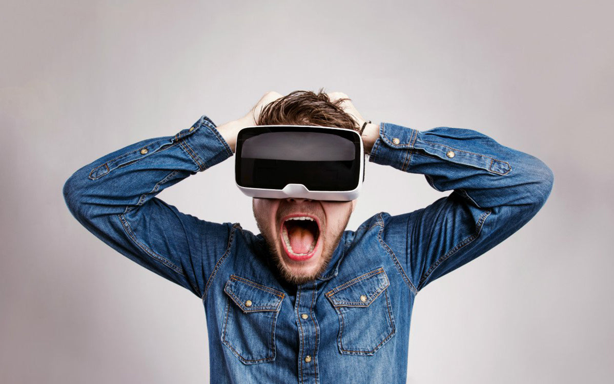 一位男士穿着牛仔衣，戴着虚拟现实头盔，张开嘴巴，看起来非常兴奋和惊讶，可能是在体验虚拟现实中的内容。