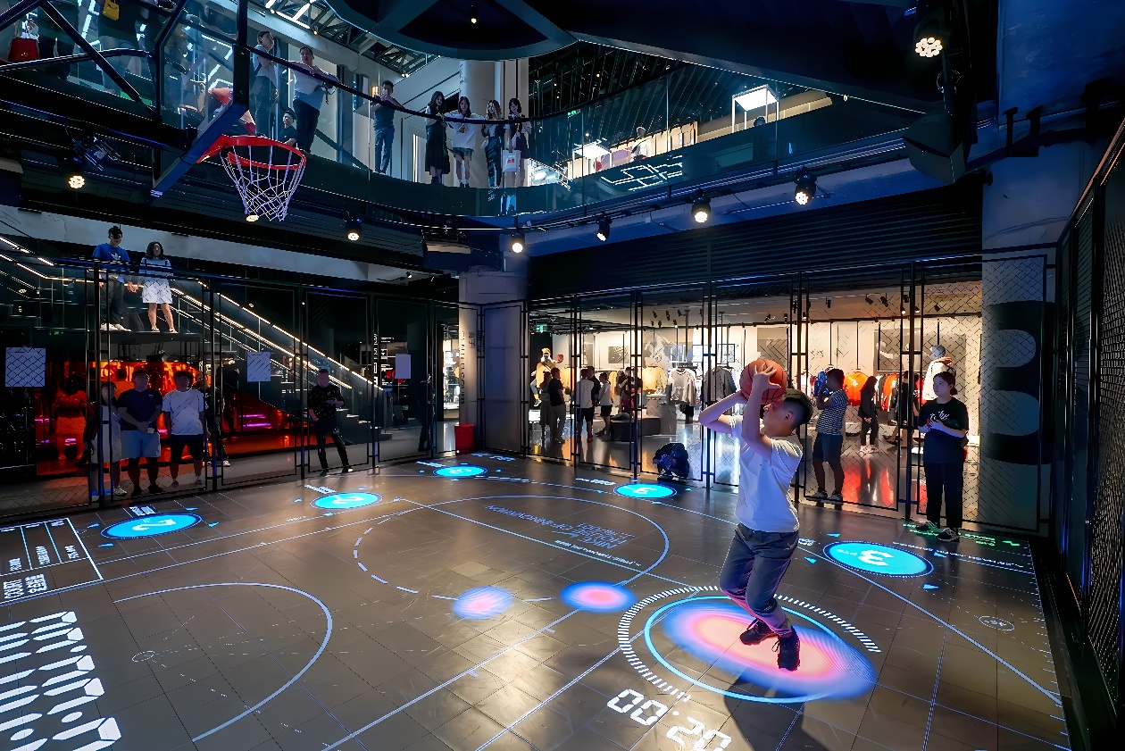 图片展示一名男子在室内篮球场上投篮，场地上有互动式地面显示屏，旁边有人观看，环境现代科技感强。
