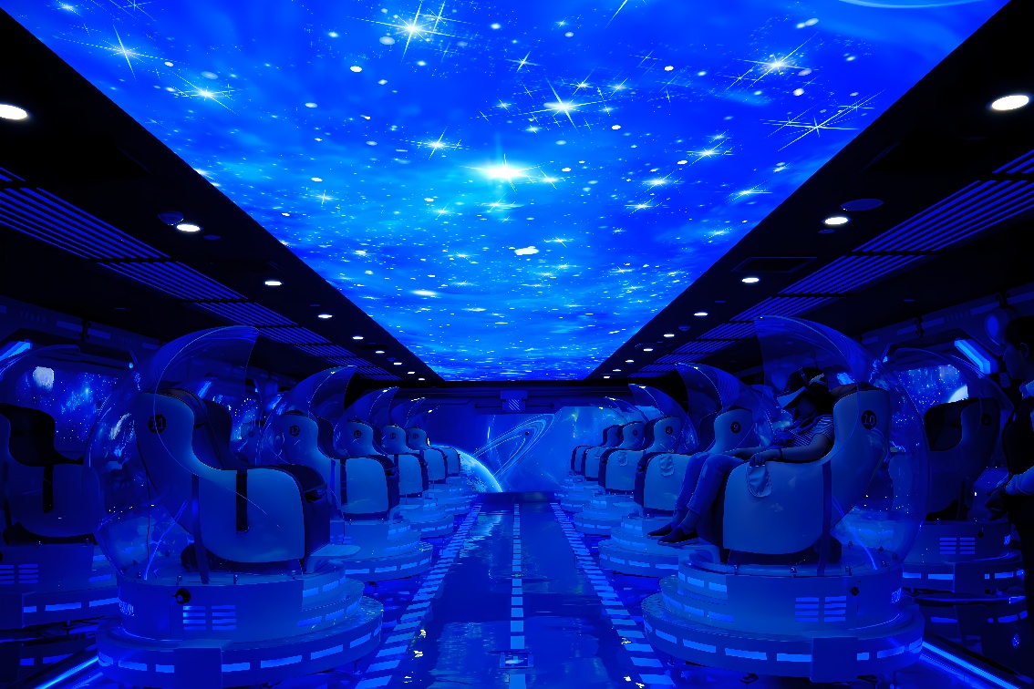 这是一张室内模拟太空舱的图片，天花板上有星空投影，两侧排列着多个现代化的模拟航天椅，整体色调为蓝色。