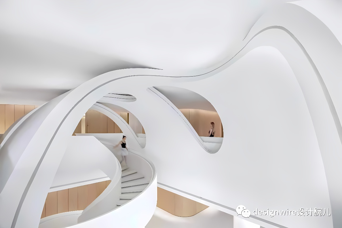 图片展示了一个现代室内设计，以流畅的白色曲线墙面为特色，有人在楼梯上行走，整体给人以未来感和艺术氛围。