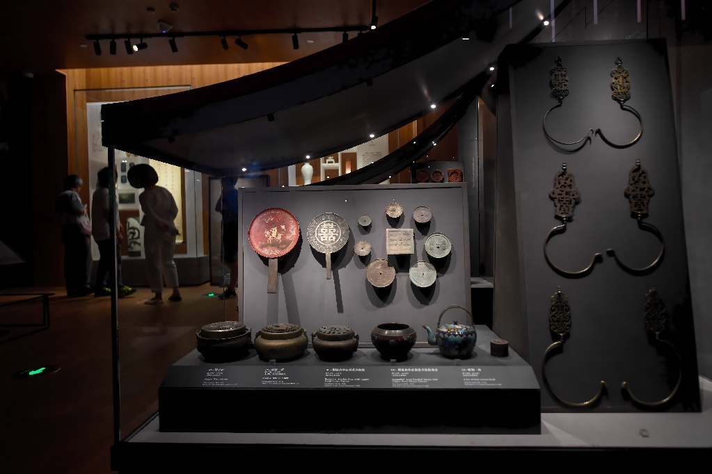 图片展示了博物馆内的展柜，陈列着古代金属器物和陶瓷，背景中有参观者在观看展品。