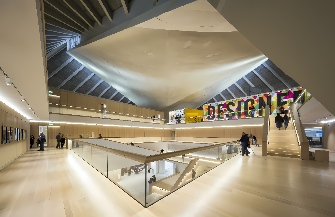 这是一张现代建筑内部的照片，展示了宽敞的空间、简洁的设计、楼梯和几位参观者。墙上有“DESIGN”字样的标牌。