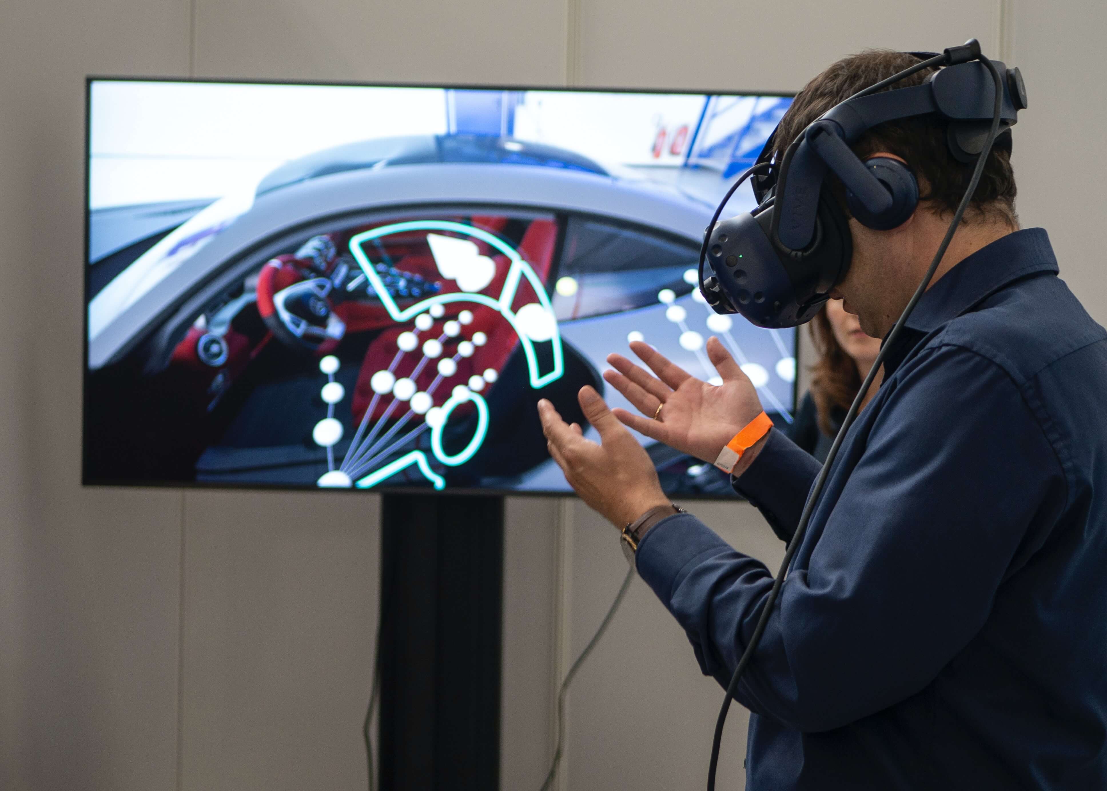 图片展示一位佩戴虚拟现实头盔的男士在模拟环境中进行互动，屏幕显示汽车内饰的三维图像。