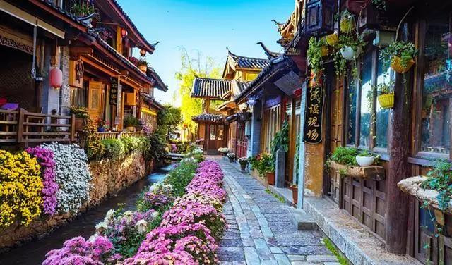 这是一条充满鲜花的古镇小巷，两旁是具有传统风格的建筑，小巷中央有一条清澈的小河流过。