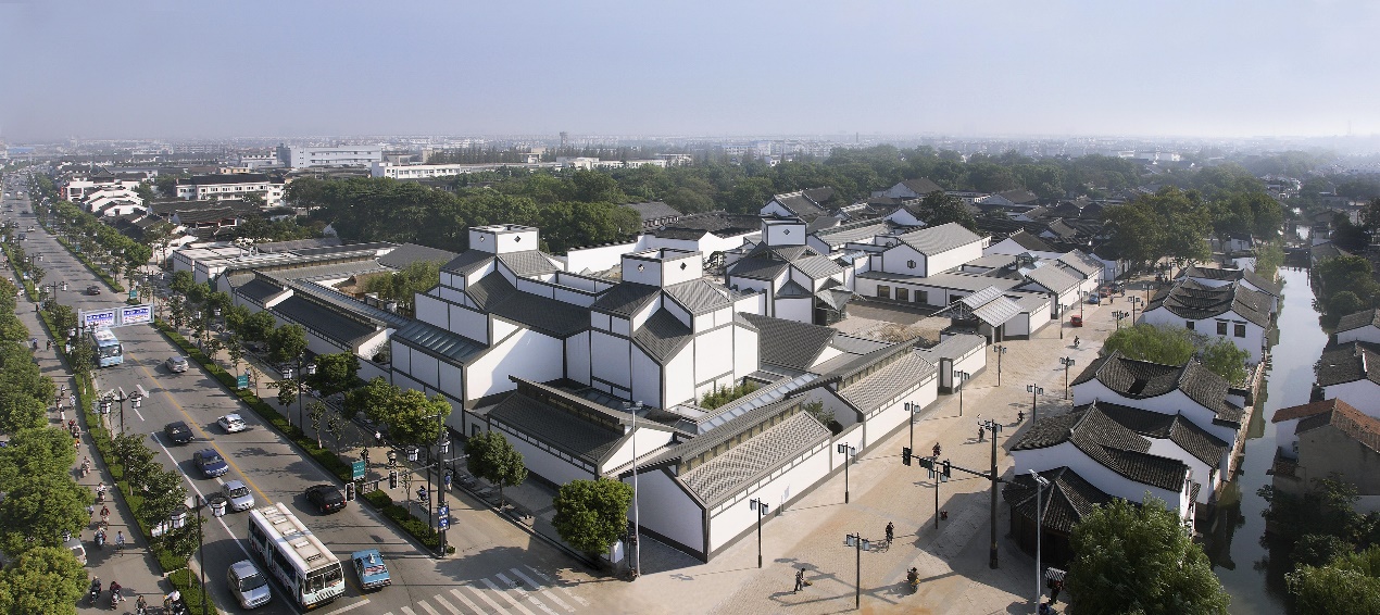 图片展示了一座具有传统风格的建筑群，周围有现代道路和车辆，远处是现代城市建筑的轮廓。