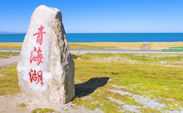 图片展示一块刻有红色汉字的巨石，背景是湛蓝的天空与海洋，地面覆盖着绿色植被。