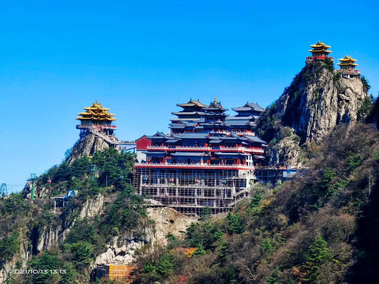 图片展示了一座位于山顶的古色古香的寺庙，寺庙建筑色彩鲜明，背靠着苍翠的山峦，天空湛蓝。