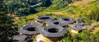 图片展示了几座圆形土楼，它们的屋顶呈现黑色，四周环绕着绿色的山丘和树木。