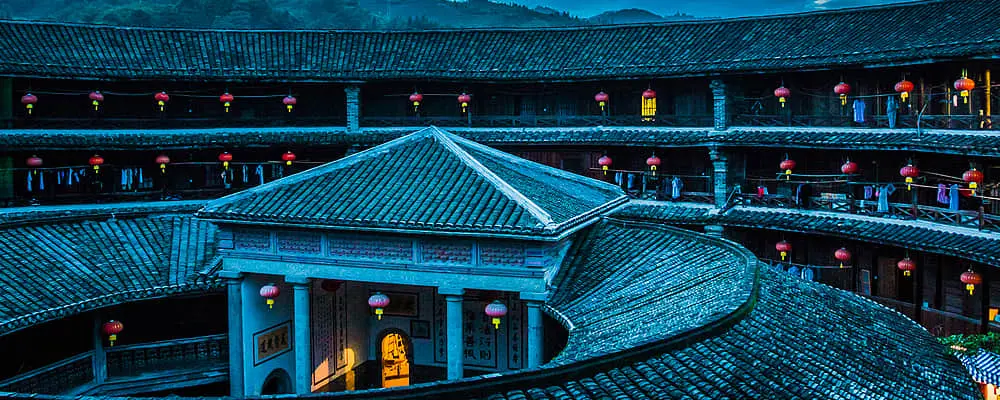 图片展示的是中国传统的土楼夜景，灯笼点缀其间，呈现出古朴和谐的氛围。