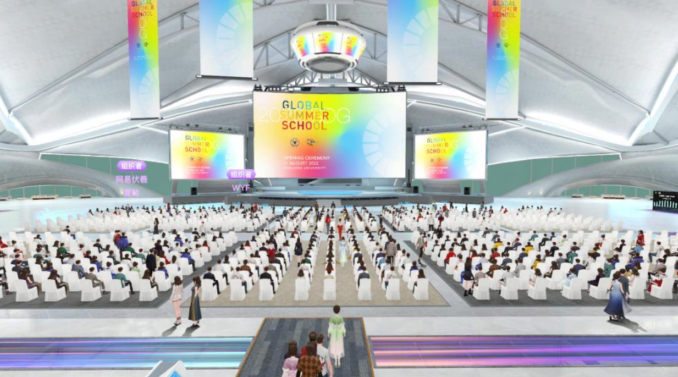 图片展示了一个宽敞的现代会议中心，人们坐在白色椅子上，前方是一个写着“GLOBAL SUMMER SCHOOL”的大屏幕。