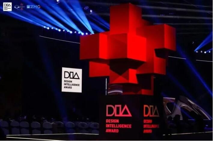 图片展示了一个设计奖项的舞台，中央有个巨大的红色十字形奖杯，周围是灯光和DIA的标志。