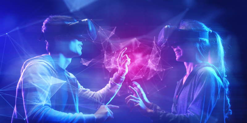 图片展示两人戴着虚拟现实头盔，似乎在体验虚拟世界，彼此用手触碰，周围有光线和数字化图形。