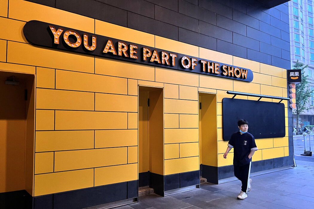 图片展示一面写着“YOU ARE PART OF THE SHOW”的墙，墙面黄黑色，一位穿蓝衣服的人从旁边走过。