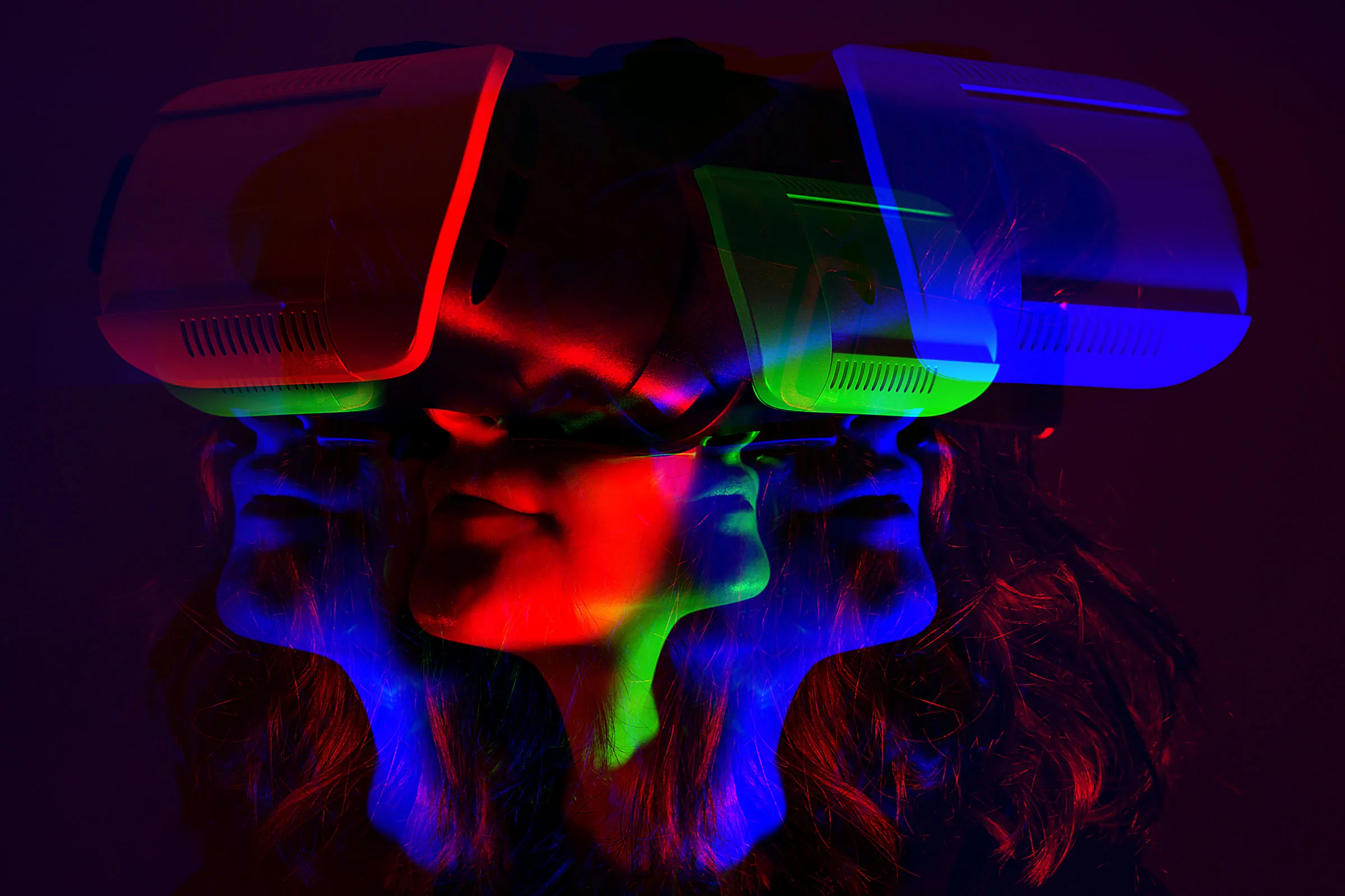 图片展示了一位佩戴虚拟现实头盔的人，头盔发出红蓝光影，形成了三重重叠的面孔错觉。