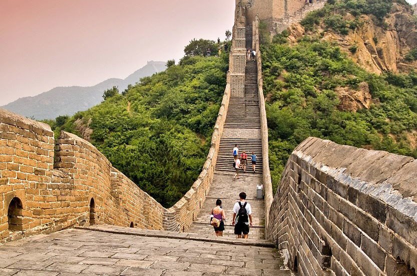 图片展示几位游客在中国著名的长城上行走，天空略显阴沉，长城蜿蜒伸展，古老砖石显露沧桑感。