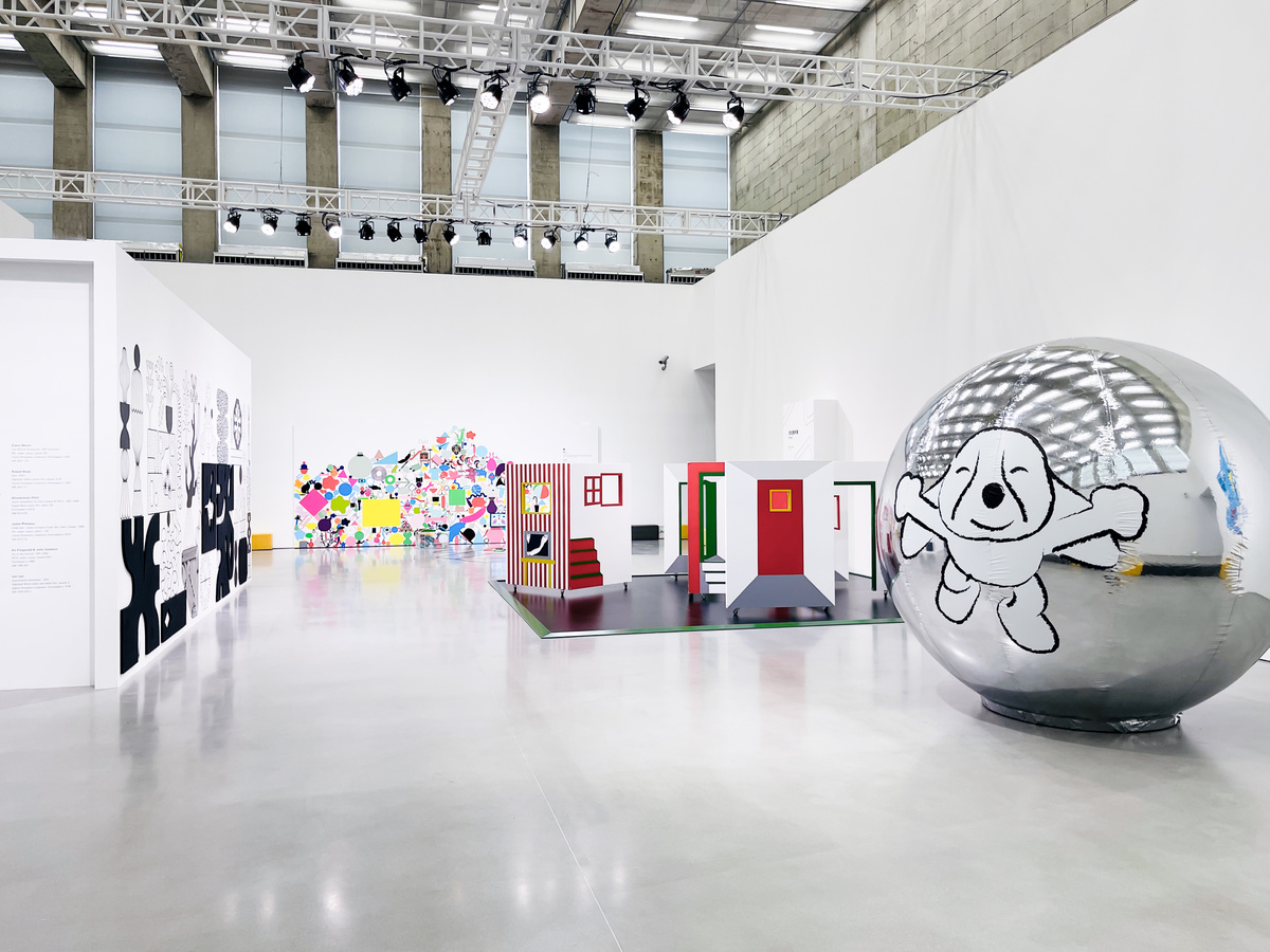 这是一间现代艺术画廊，墙上挂着多彩艺术作品，展厅宽敞明亮，中间有一个巨大的银色球体装置。
