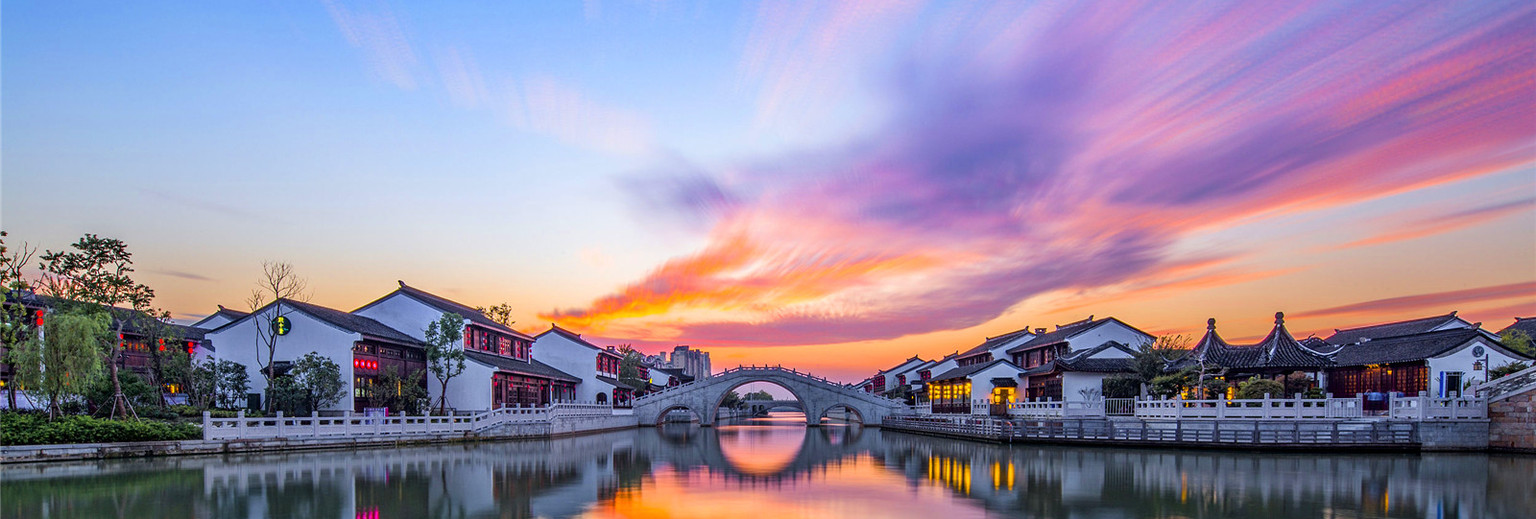 这是一张展示中国传统建筑与拱桥的风景照片，天空中绚丽的晚霞与水面倒影相映成趣，呈现出宁静美丽的氛围。