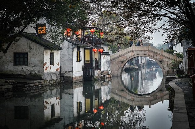 图片展示了中国古镇的一角，有拱桥、古建筑和水面倒影，显出宁静古朴的氛围。几盏红灯笼增添了节日气氛。
