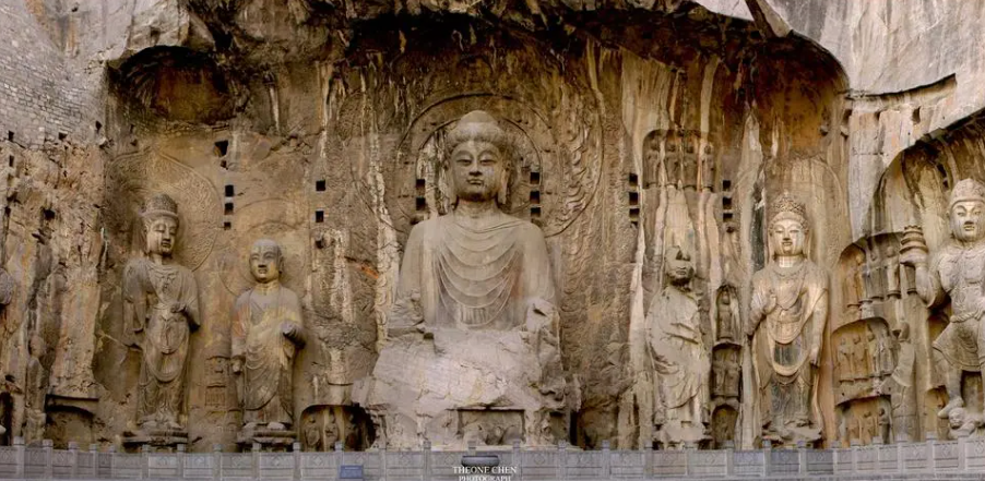 这是一组雕塑，中间是一尊巨大的佛像，两旁有较小的佛像，背景是岩石，可能是石窟中的艺术作品。