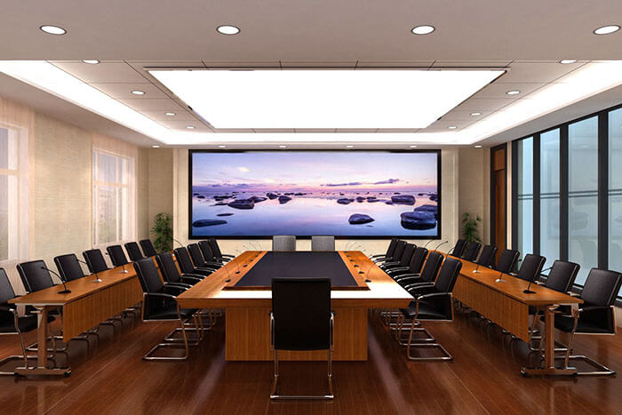 这是一间现代会议室，配有长型会议桌、黑色会议椅和一面展示海滩风景的大屏幕。室内设计简洁明亮。