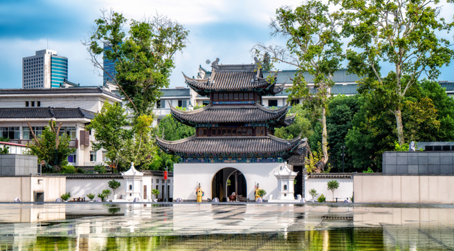 这是一幅展示中国传统建筑的图片，有屋檐翘角的亭子，前有水池，背景是现代建筑，融合了古典与现代风格。