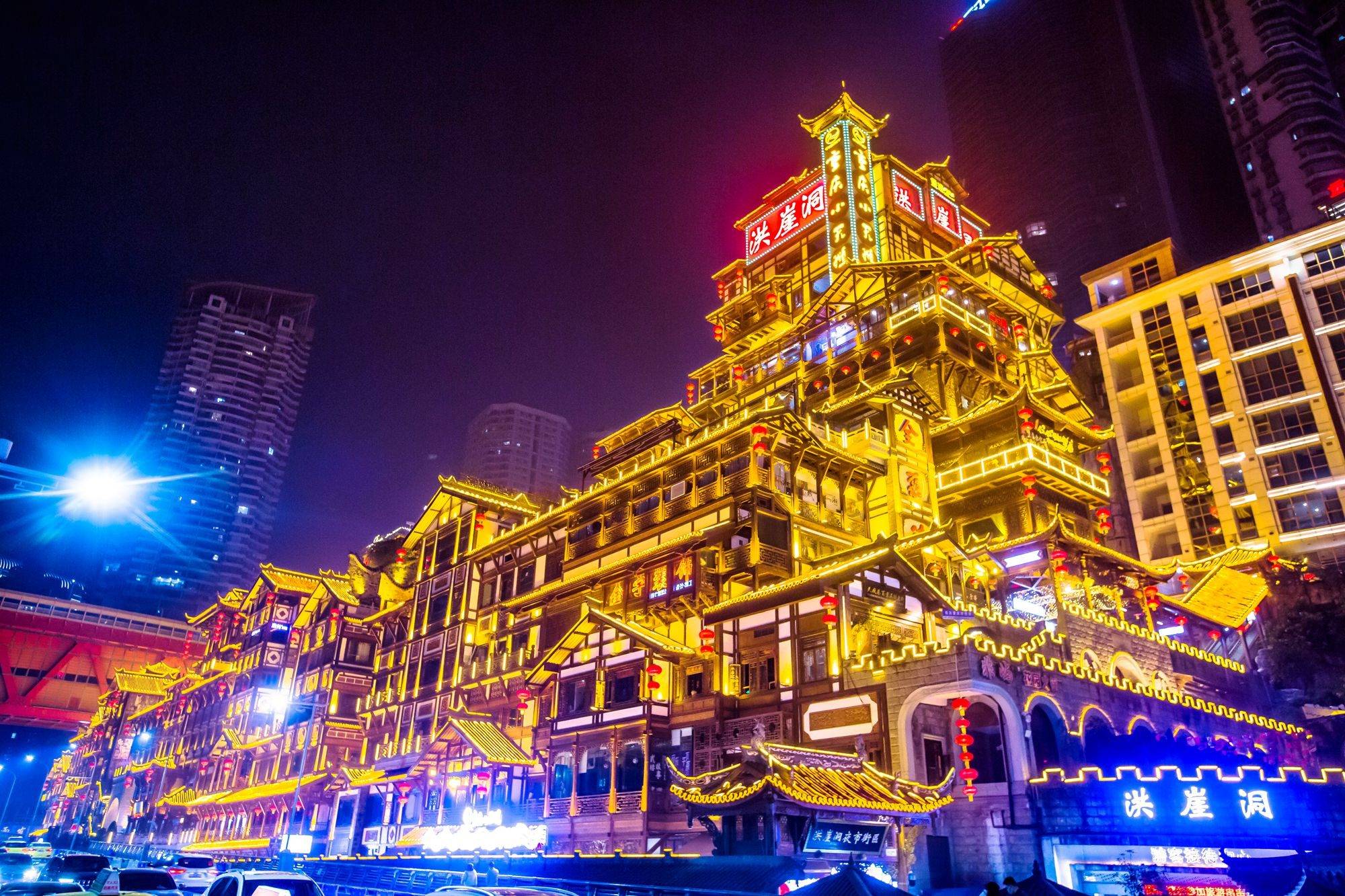 这是一张展示夜晚灯光璀璨的中国传统建筑照片，建筑物金色灯光映衬，与现代高楼大厦形成鲜明对比。