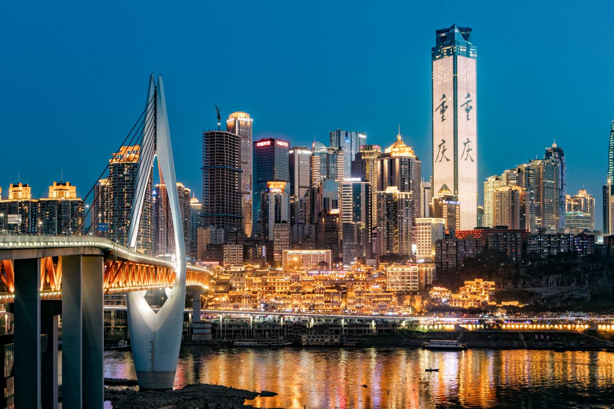 这是一张城市夜景照片，展示了一座现代化大桥和背后繁华的高楼大厦，灯光璀璨，映照在河流之上。