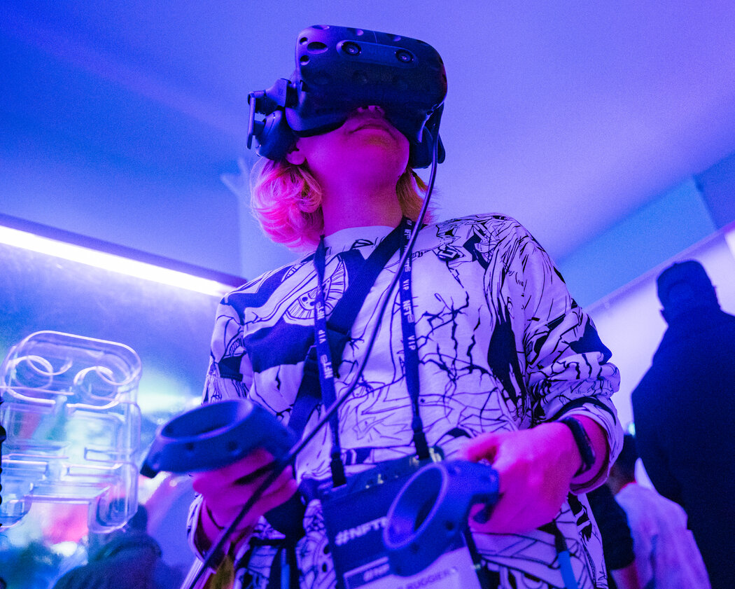 图片展示一位戴着虚拟现实头盔的人，双手持有控制器，似乎正在体验VR游戏，四周灯光昏暗，氛围科技感十足。