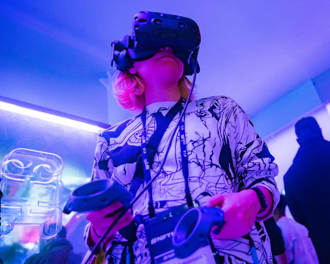 图片展示一位戴着虚拟现实头盔的人，手持控制器，似乎在体验沉浸式VR游戏。背景是紫蓝色灯光照亮的房间。