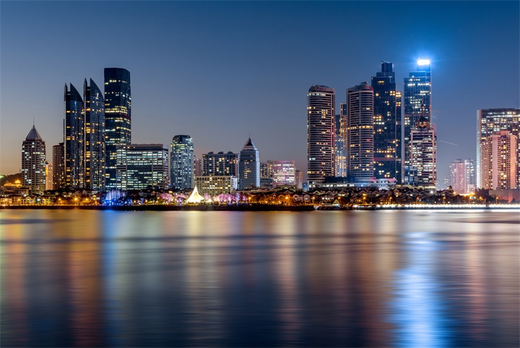 这是一张城市天际线的夜景照片，高楼大厦灯火辉煌，倒映在平静的水面上，呈现出宁静而现代的氛围。