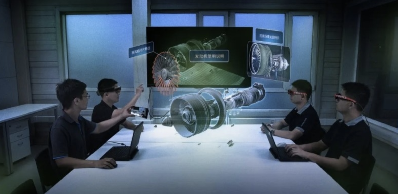 图片展示了四位佩戴眼镜的人围坐一桌，前方是一块展示机械部件图解的大屏幕，似乎在进行技术讨论或学习。