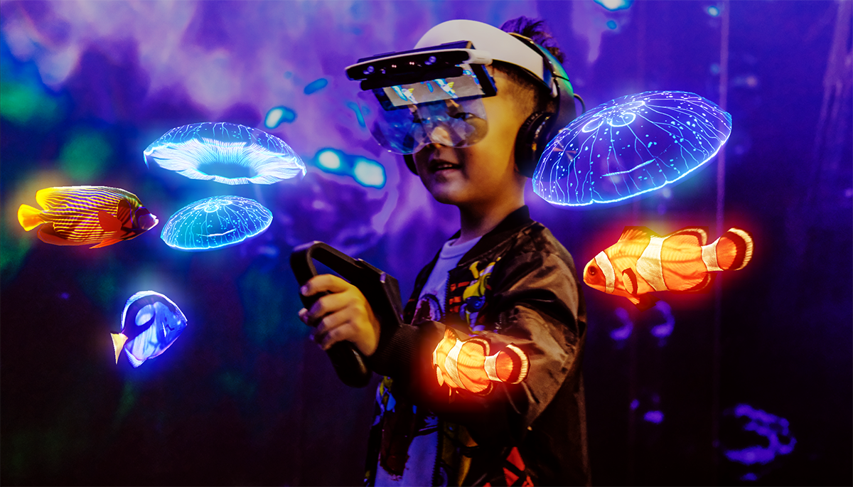 一位小孩正戴着虚拟现实头盔，专注地体验着虚拟世界中的水母和热带鱼，周围光影斑斓，如梦似幻。