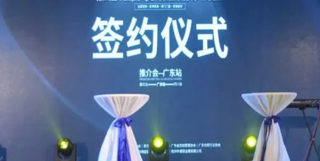 图片展示了一个舞台背景，上面写着“签约仪式”四个大字，旁边有两个装饰布艺的桌子，灯光映照下氛围庄重。