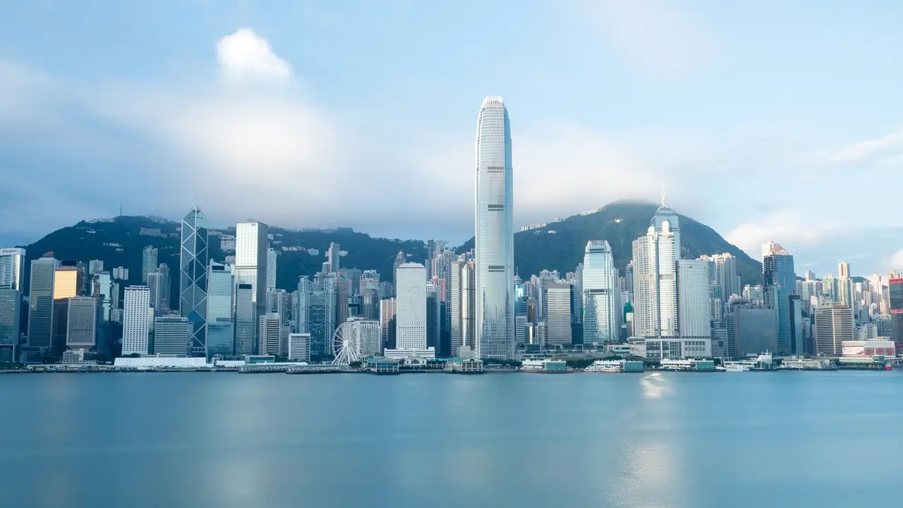 这是一张香港天际线的照片，展示了维多利亚港，高楼大厦林立，天空呈现出宁静的蓝色，云彩飘渺。