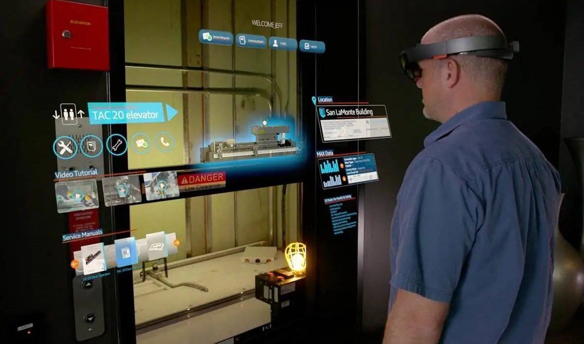 图片展示一位男士戴着增强现实眼镜，眼前浮现多个虚拟信息界面，背景为工作环境，看似正在进行某种交互式操作。