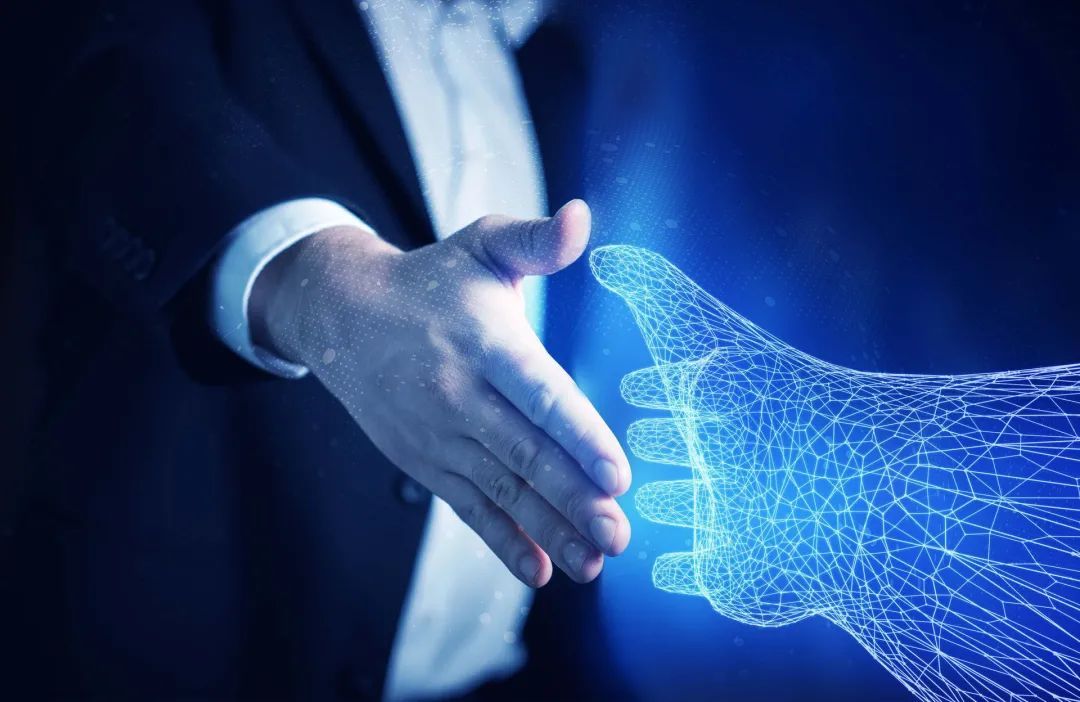 图片展示了一位穿着正装的人伸出手与一只由蓝色光线构成的数字化虚拟手进行握手，象征着现实与数字世界的结合。