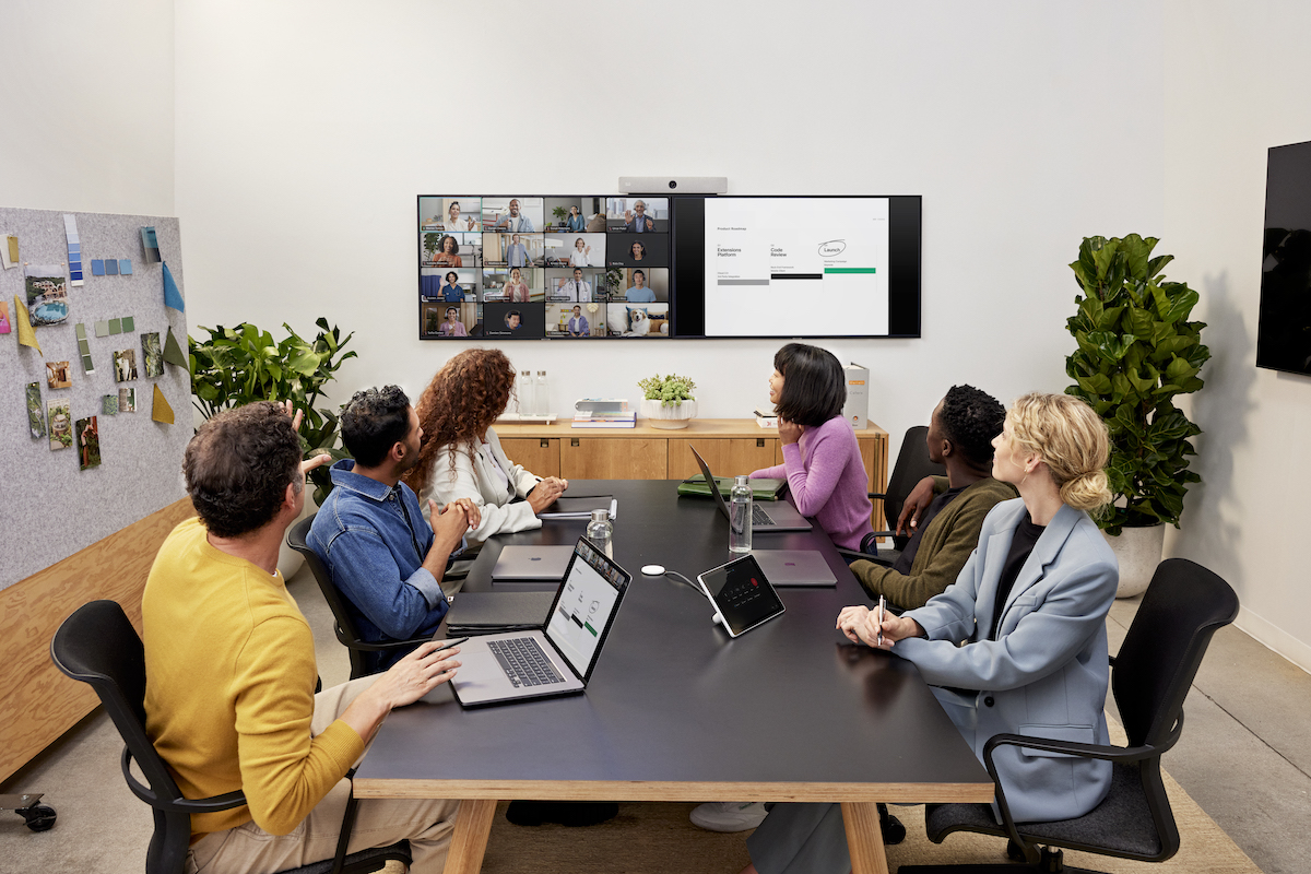 图片展示几人围坐会议桌，注视着前方屏幕，屏幕显示远程会议参与者，办公环境现代，氛围专业。