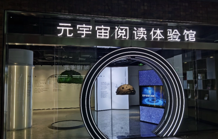 图片展示了一个现代感的展览入口，上方有“元宇宙的探险体验”字样，入口设计成圆形门洞，内部可见展品和屏幕。