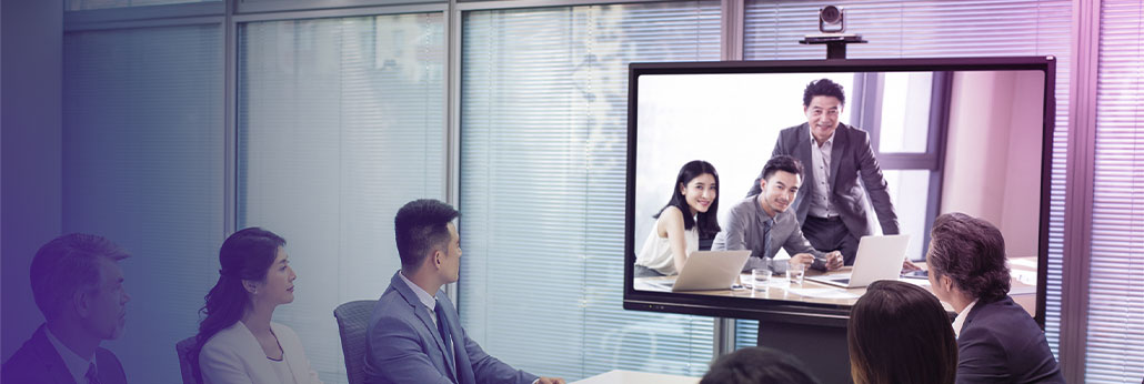 图片展示了一间会议室内的场景，几名职员正专注地观看屏幕上的视频会议，视频中有三人正在讨论。